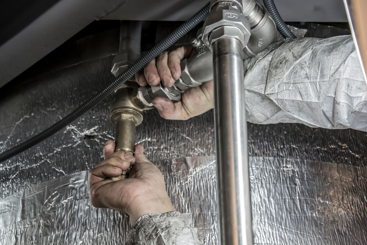 Hands fitting pipework under a sink